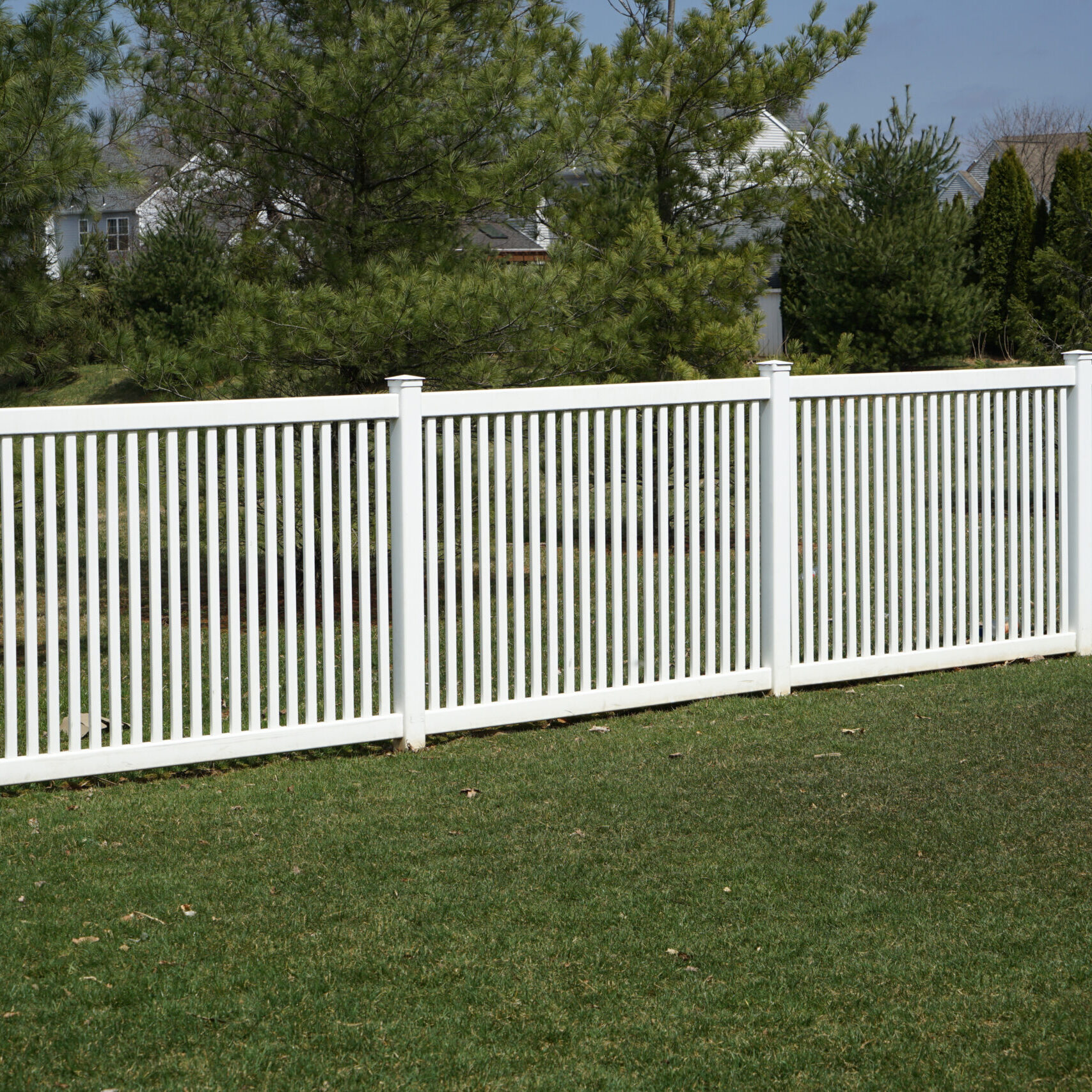 A new white vinyl fence by a grass area with trees behind it.